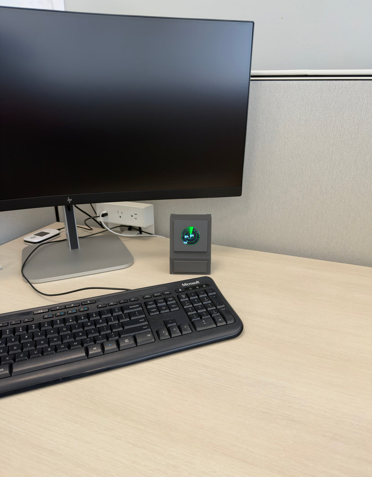 DeskSpotter on a desk behind a full-size keyboard and beside a monitor, showing its true size